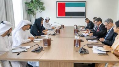 A group of delegates from India and the UAE engaged in a formal meeting, seated around a conference table with microphones, documents, and a UAE flag in the background.