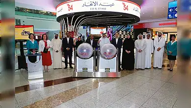 A group of Dubai Duty Free officials and guests stand beside the Millennium Millionaire and Finest Surprise draw machines at Dubai International Airport.