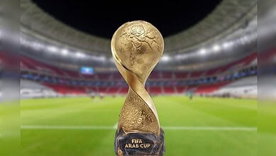 The FIFA Arab Cup trophy displayed on a football pitch inside a brightly lit stadium.