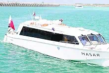 A white passenger ferry named MASAR, carrying the Qatari flag, sails through turquoise waters at Al Ruwais Port in Qatar.
