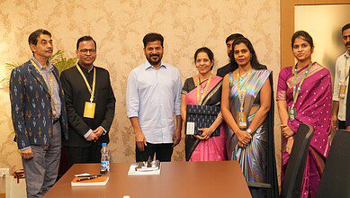 Seven professionals standing together in a conference room for a group photo, several wearing traditional Indian attire and conference badges