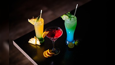 Glasses of colourful sweetened beverages served with fruit garnishes.