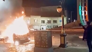 This frame grab from a video released Friday, January 9, by Iranian state television shows a man holding a device to document burning vehicles during a night of mass protests in Zanjan, Iran.