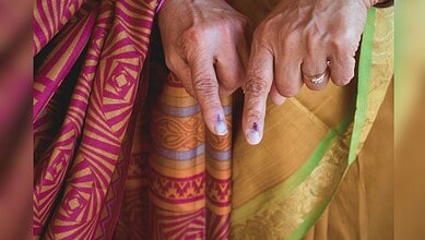 image shows two people wearing a colorful traditional sari and displaying fingers marked with ink, indicating they have voted in an election.