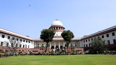 View of the Supreme Court of India with lush green lawn and trees in front.