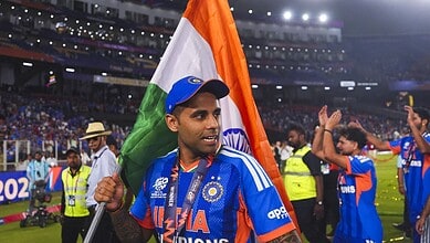 Suryakumar Yadav holding the Indian flag after a cricket match victory, surrounded by teammates and fans.