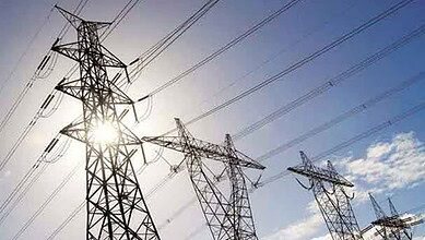 High-voltage power lines on transmission towers against a sunny sky.