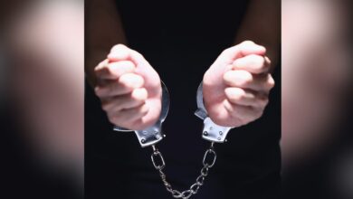 Close-up of two clenched fists bound together by silver metal handcuffs against a dark background.