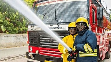 Firefighters training with a fire hose in front of a fire truck.
