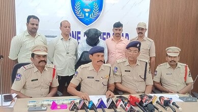 Arrested man in Hyderabad for Rs 10L bank loan fraud, surrounded by police officers during a press confer.