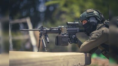 Soldier aiming IWI Negev 7 light machine gun in outdoor setting.