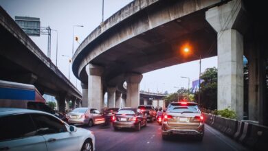 Image shows Cars stuck in heavy traffic under a multi-level concrete highway interchange at dusk.
