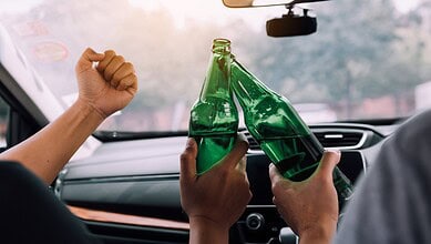 Celebrating with cheers and clinking green glass bottles inside a car during a festive occasion.