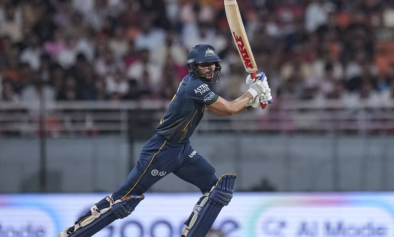 A young cricket player in action during a match, wearing a navy blue uniform and helmet, with a crowd wat.