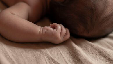 Close-up of a sleeping newborn baby with tiny hand curled near face.