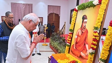 A man paying homage to a large framed portrait of a revered spiritual leader at a ceremonial event.