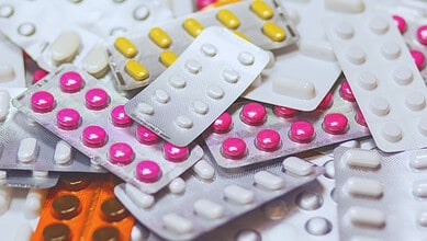 Blister packs containing various pills, including pink, yellow, and white tablets, scattered on a surface.