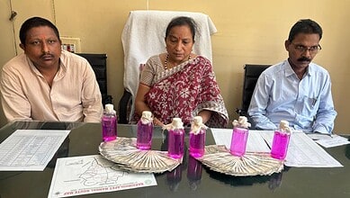 A woman and two men seated at a table with bottles of pink liquid and documents, in an indoor setting.