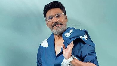Man with glasses and a beard wearing a blue shirt, holding a jacket over his shoulder.