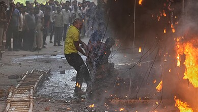 A man fighting fire during a protest with flames and smoke in the background.