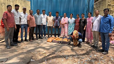 Group of people standing outdoors with a woman kneeling on the ground in front of bags of food.