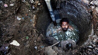 Man trapped in a deep, narrow sewer well with water up to his chest.