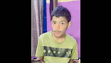 A young boy with dark hair and a light green t-shirt standing indoors against a purple wall.