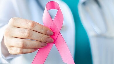 Pink ribbon for breast cancer awareness held by a healthcare professional.