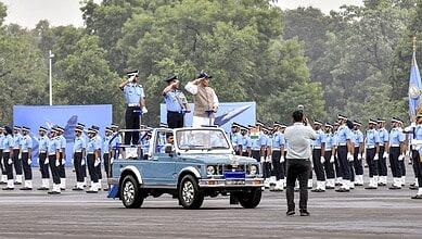 Air force officers saluting during a formal parade with a vintage vehicle in the foreground, outdoor sett.