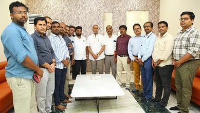 A diverse group of men gathered around a table in an office setting, posing for a group photo.