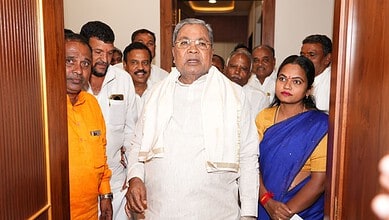 Senior man in white traditional attire with a group of people, including a woman in a blue saree, standin.