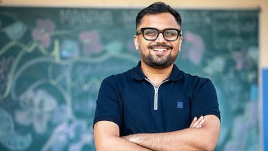 Smiling male teacher in front of a chalkboard with drawings and equations.
