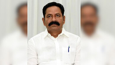 A man with a mustache wearing a white shirt, standing against a light background.