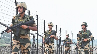 Indian paramilitary soldiers patrolling along a barbed wire fence, equipped with rifles and protective ge.