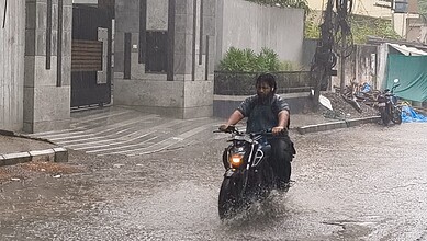 Motorcyclist navigating through flooded street during heavy rain in an urban setting.