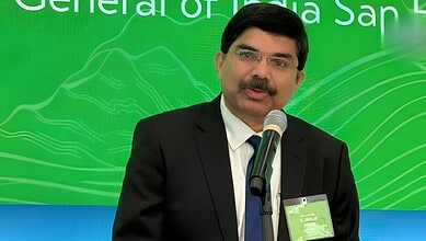 Srikar Reddy speaking at a conference with a green backdrop.