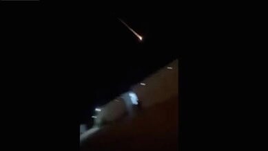 Bright meteor streaks across a dark night sky over a cityscape.
