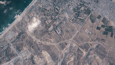 Aerial view of a large earthen barrier construction inside Gaza, with surrounding fields and urban areas.