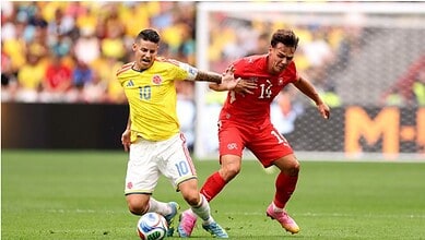Two soccer players competing for the ball during a match, one in yellow and the other in red.