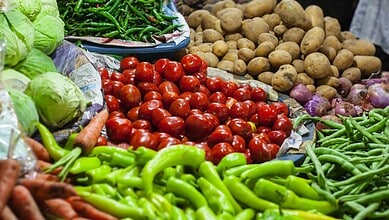 Fresh vegetables including tomatoes, potatoes, green beans, and lettuce at a market stall.