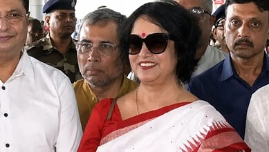 Taslima Nasreen in a white saree with red border, wearing sunglasses, smiling among a crowd in Kolkata.