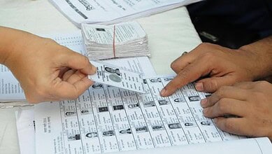 Voters' identification process during an election in India, with ballot papers and ID cards visible.
