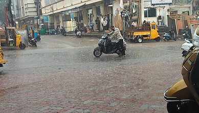 Rainy street scene in Hyderabad with vehicles and pedestrians during drizzle.