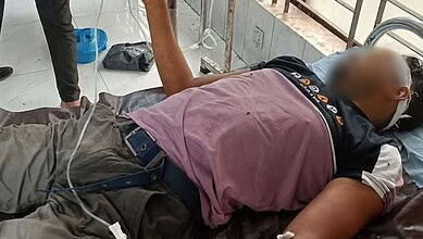 Unconscious man with oxygen mask lying on hospital bed in Bangladesh.