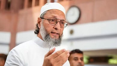 Owaisi speaking passionately, wearing white traditional attire and glasses, in a public setting.