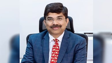 Srikar Reddy, dressed in a blue suit, smiling in an office setting, appointed as India's envoy to Qatar.