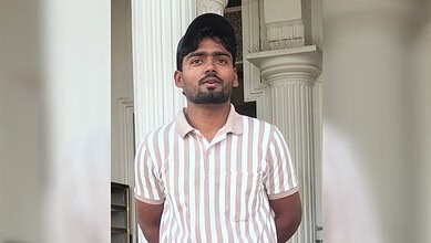 Young man in striped shirt standing outside with columns in background.
