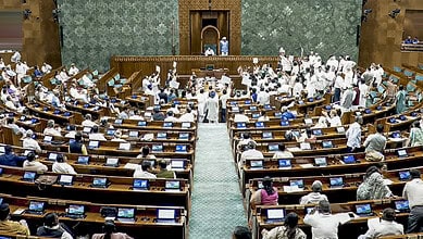 Parliament session with members engaged, some standing, in a large hall with green decor.