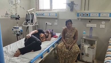 Patient lying on hospital bed with a woman sitting nearby in a hospital room.