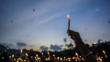 Person holding a lit candle during a memorial vigil at dusk in West Bengal.